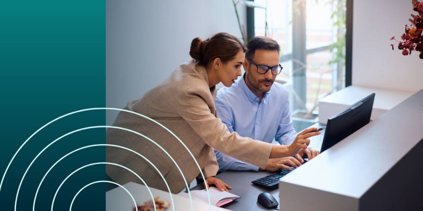 Two professionals collaborating at a desk with a computer, discussing and pointing at the screen in a modern office space.