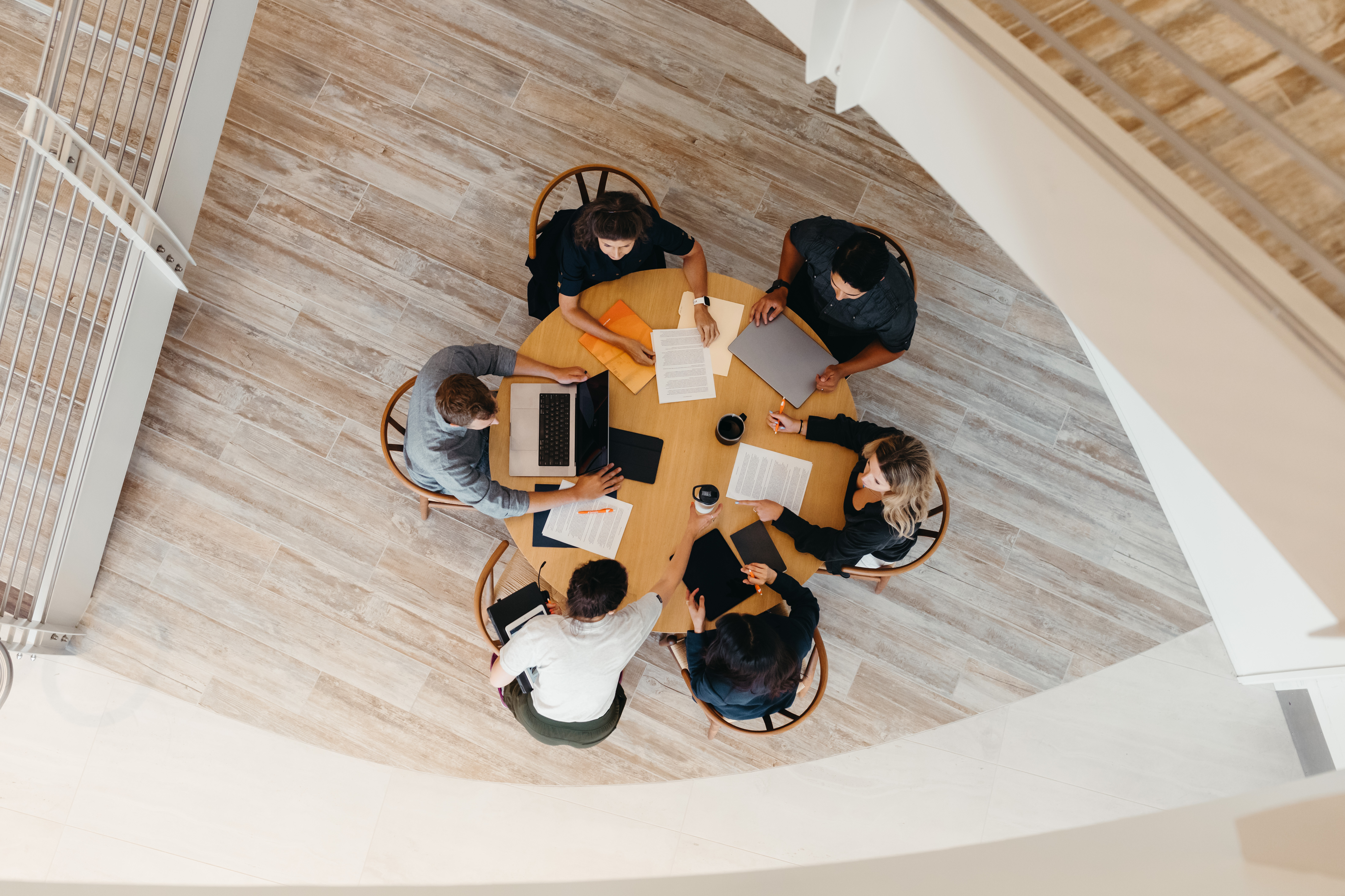 A group of people seated around a circular table engaging in a collaborative activity, viewed from above.