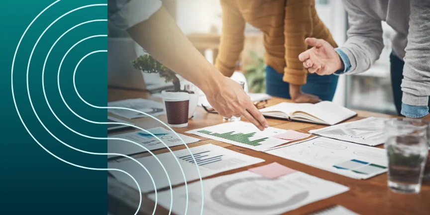 People discussing documents and graphs on a wooden table with a teal graphic overlay on the left side.
