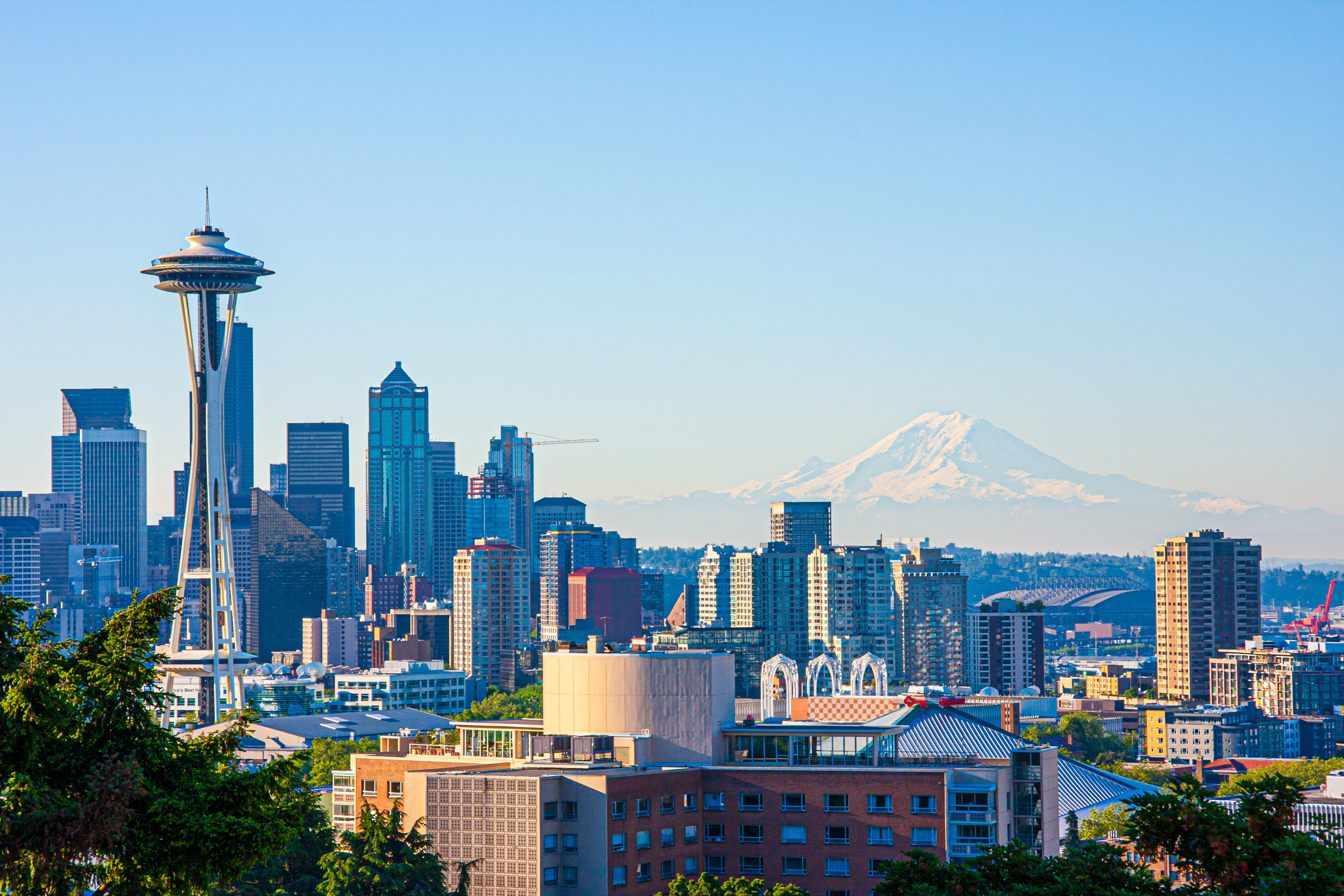 Seattle cityscape featuring the Space Needle, downtown buildings, and Mount Rainier in the distance against a clear sky.