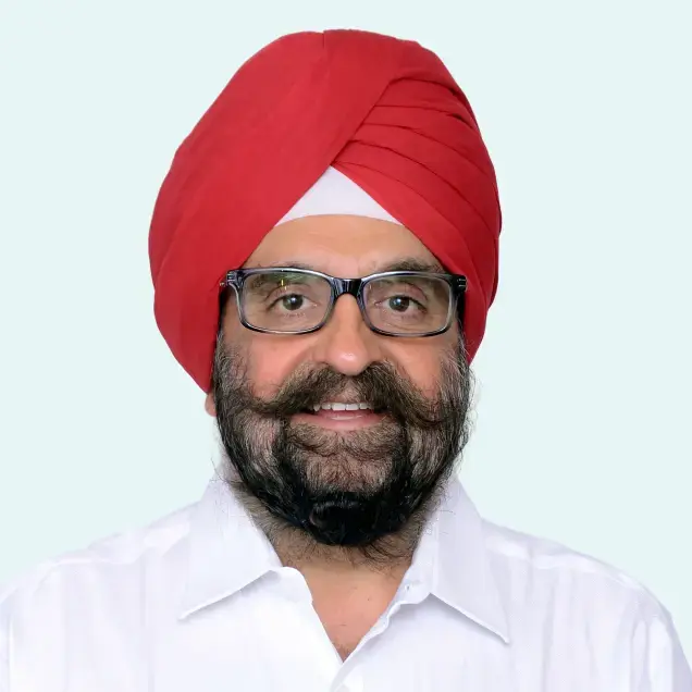 A man with glasses, a red turban, and a white shirt smiling against a light background.